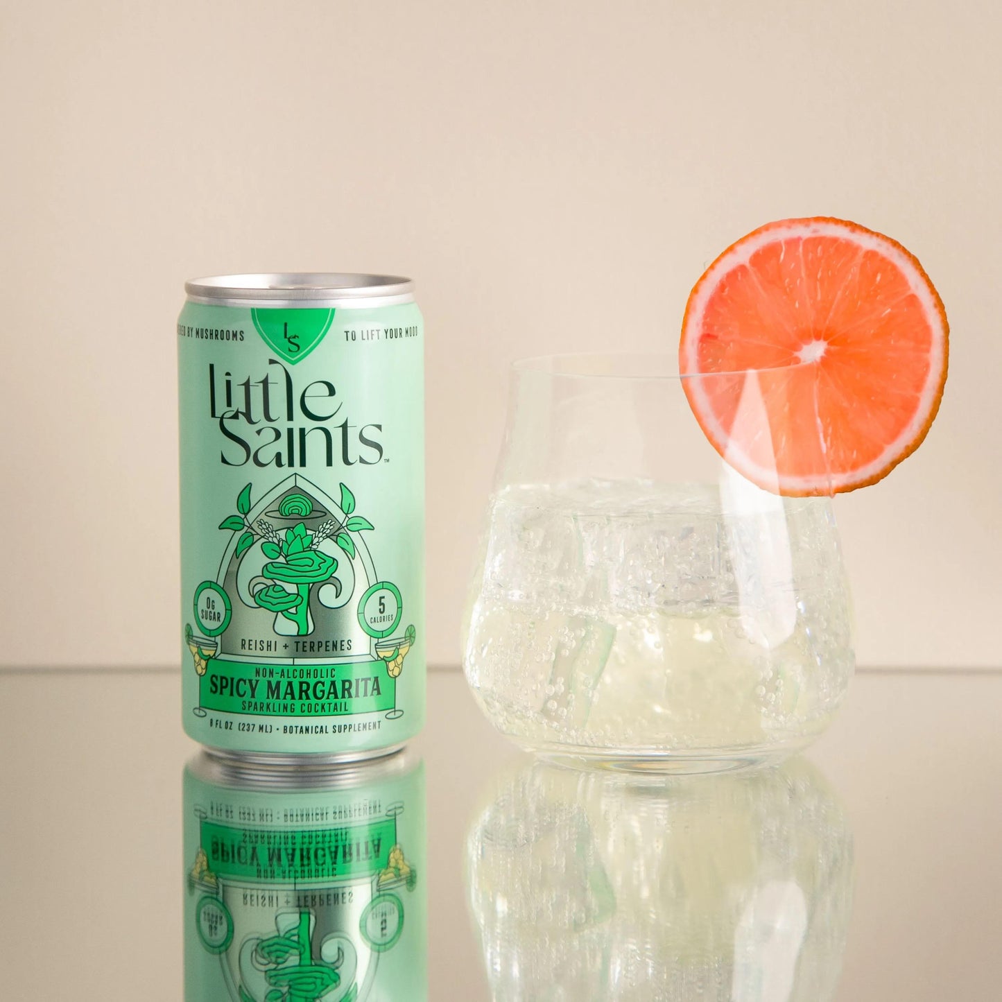 Can of Little Saints Spicy Margarita non-alcoholic cocktail next to a glass with ice and a grapefruit slice garnish.