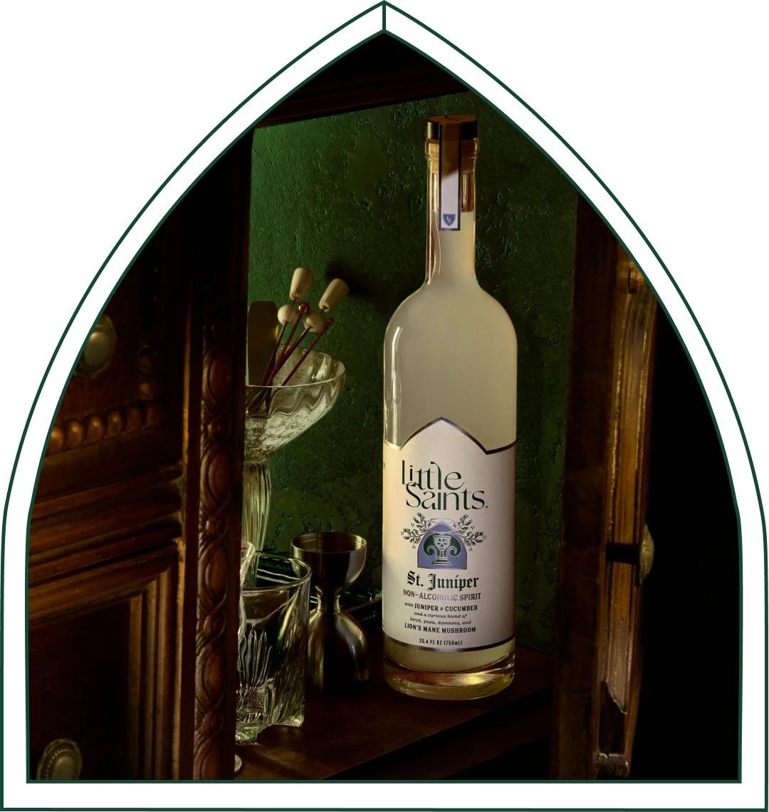 Bottle of Little Saints Saint Juniper non-alcoholic spirit displayed with glassware inside a wooden cabinet.