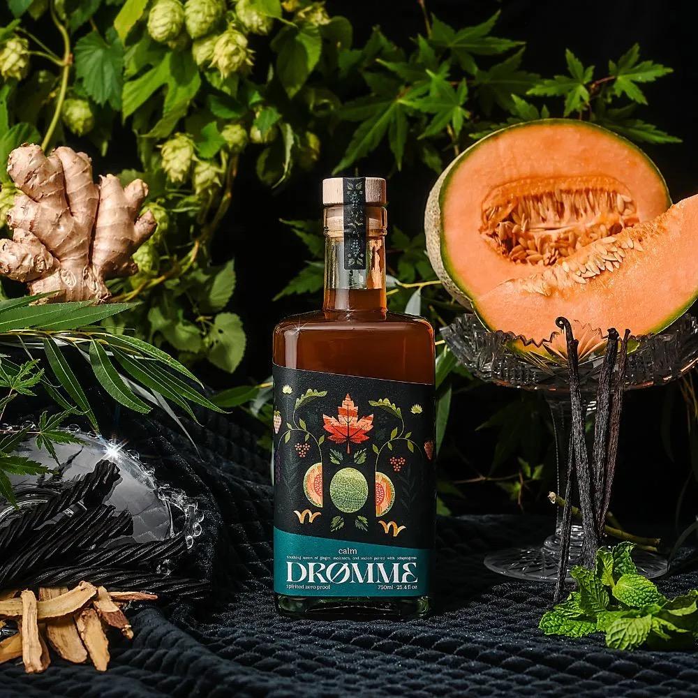 Bottle of Drømme Calm with ginger root, melon, vanilla beans, and green leaves on black fabric background