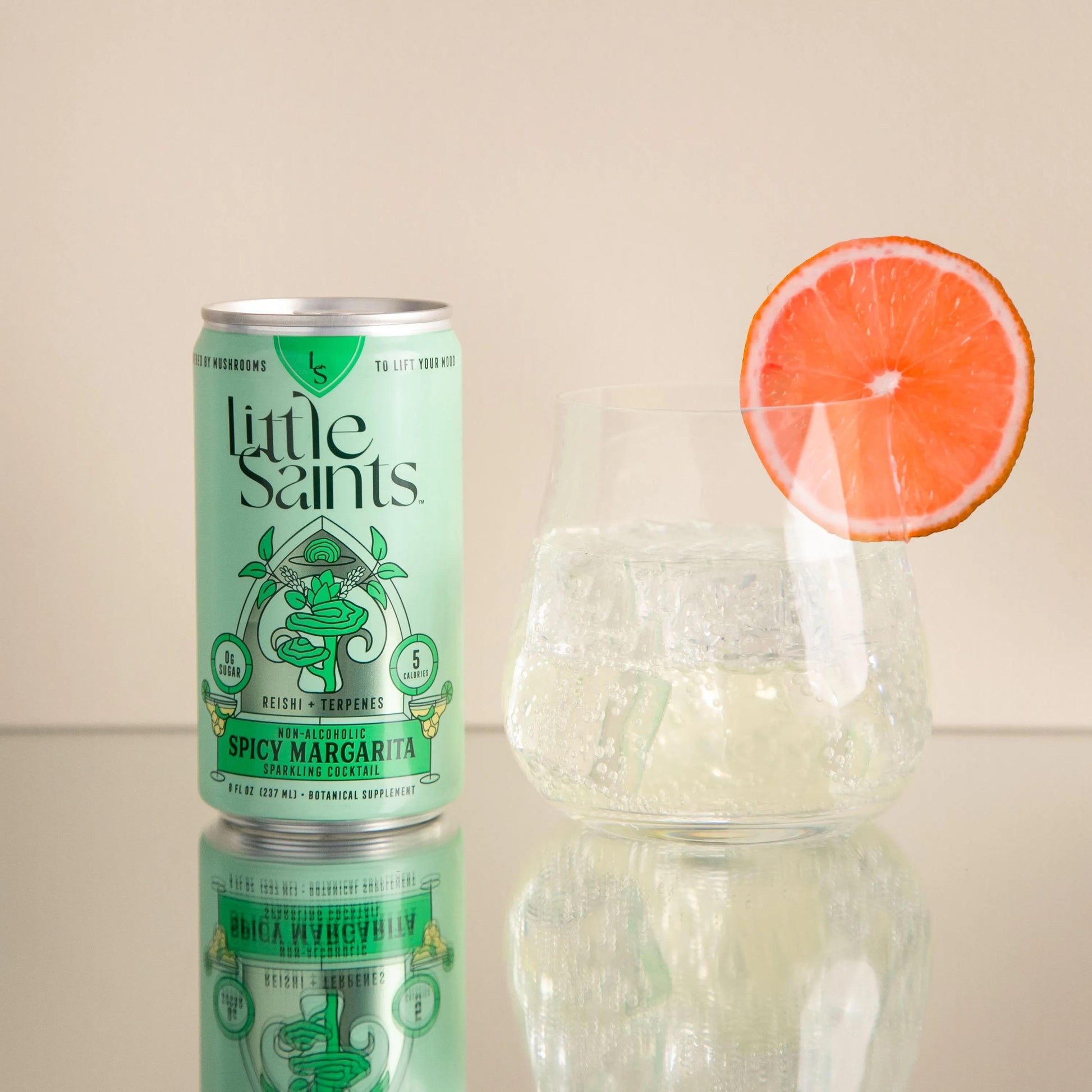 Can of Little Saints Spicy Margarita non-alcoholic cocktail next to a glass with ice and a grapefruit slice garnish.