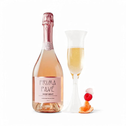 Bottle of Prima Pavé Rosé Brut sparkling wine next to a filled flute and fresh fruit on white background