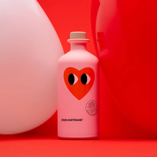 Pink Yiayia & Friends Love Edition EVOO bottle with heart design, set against red and white balloon background