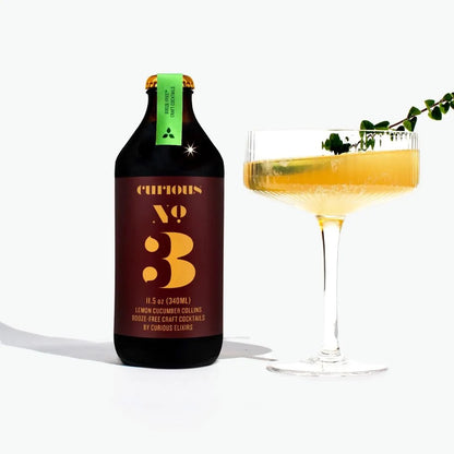 Bottle of Curious Elixirs No3 Collins and a glass with a lemon cucumber cocktail garnished with herbs