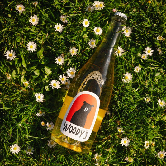 Bottle of Woody's sparkling non-alcoholic Blanc de Blanc on grass with white daisies around it