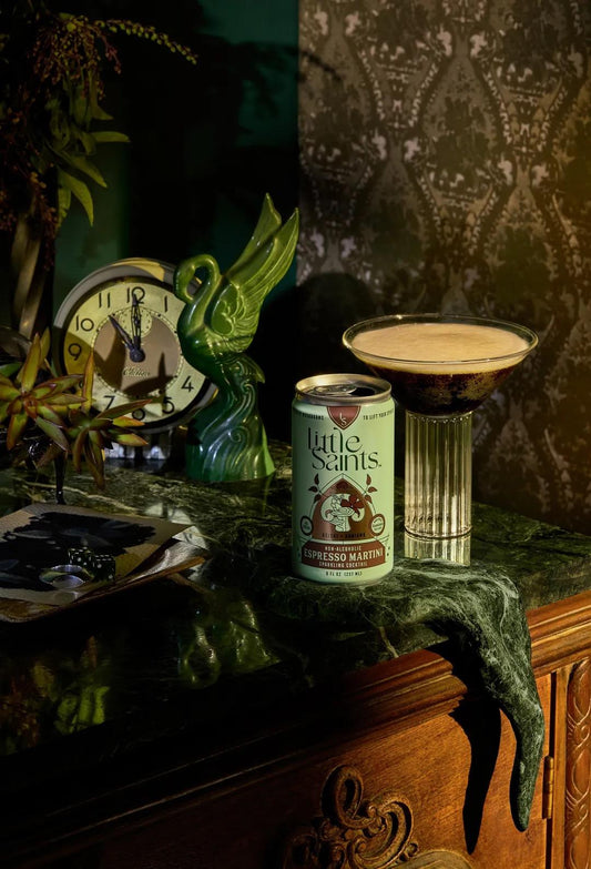 Little Saints Espresso Martini can and a prepared cocktail glass on a vintage green marble surface with decorative items and clock in background